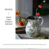 A rustic ceramic milk pitcher with a cracked glaze and pastoral design, featuring green foliage patterns.