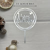 Silver acrylic cake topper with happy birthday text and heart design on a wooden surface