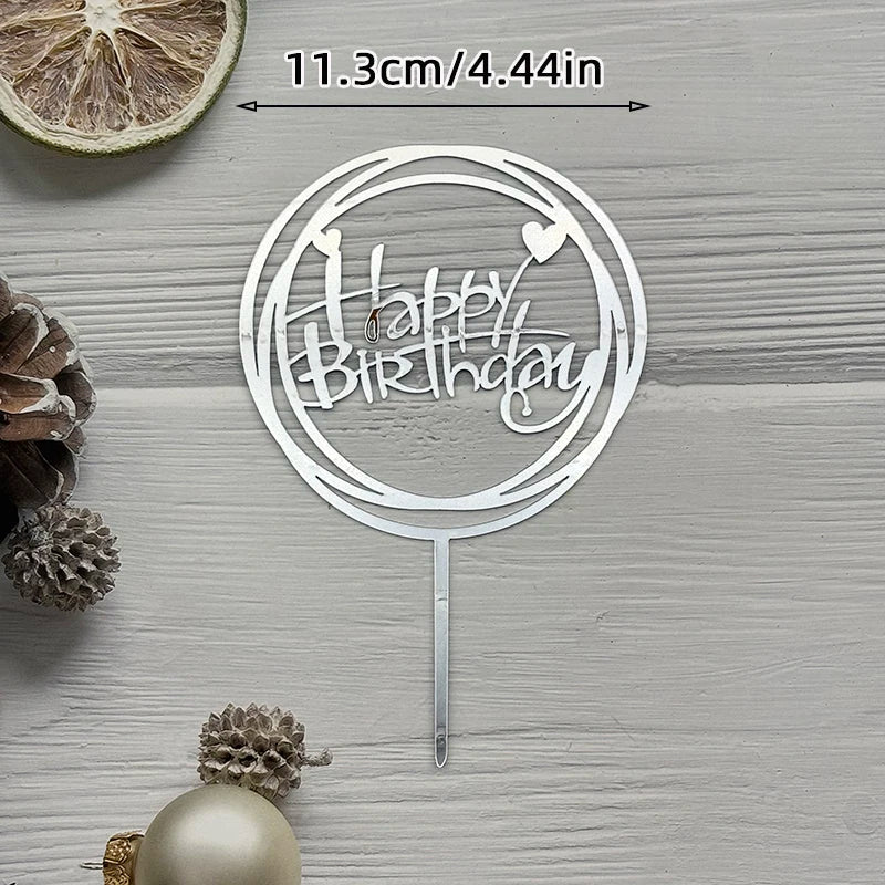 Silver acrylic cake topper with happy birthday text and heart design on a wooden surface