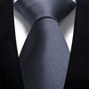A close-up shot of a dark gray silk necktie tied in a knot against a black suit jacket.