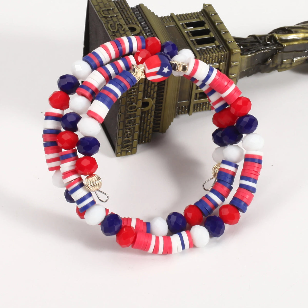 A circular bracelet made of red, white, and blue beads with stars and stripes, displayed next to a gold-colored object.