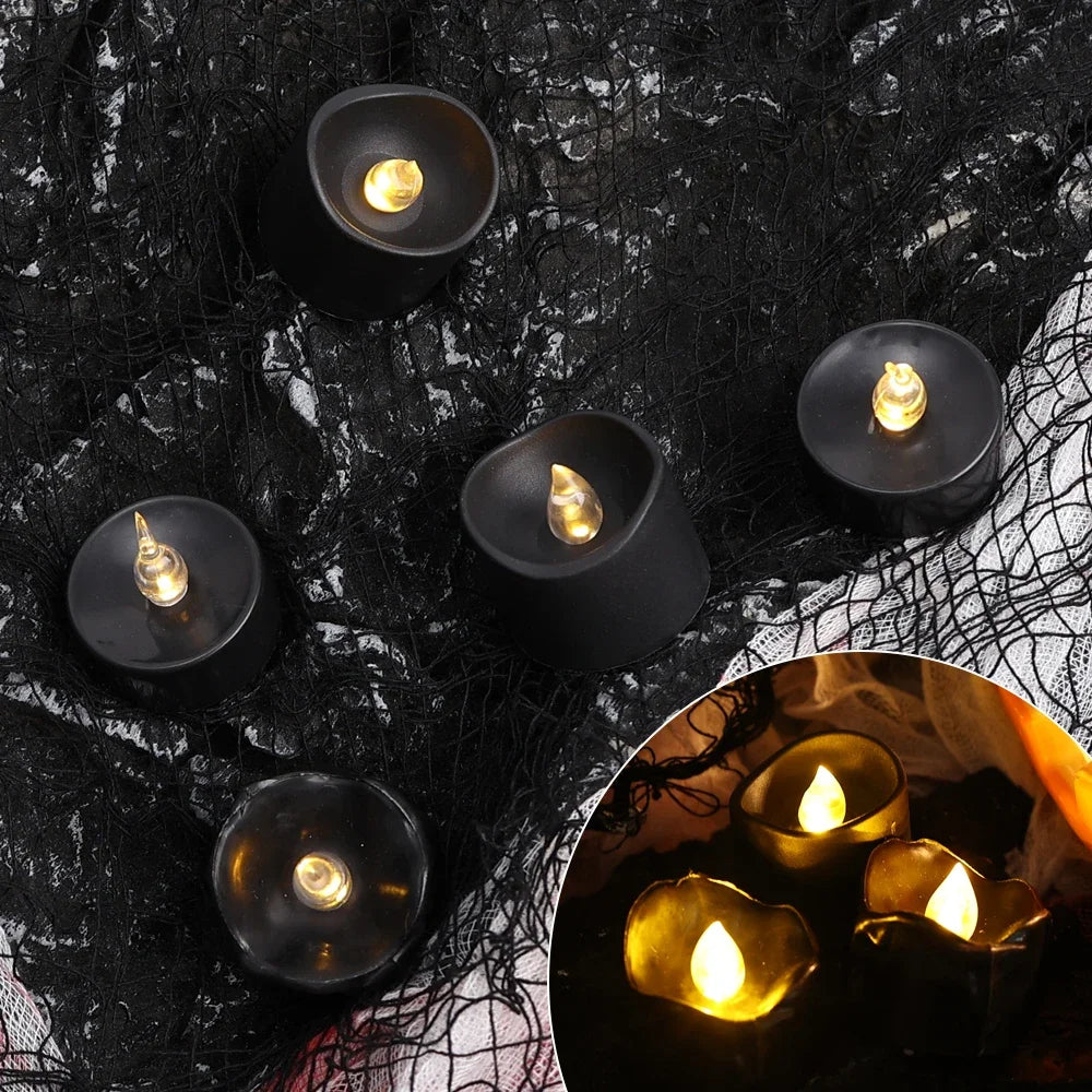 A collection of black LED candles with a warm white glow arranged on a dark, textured surface.
