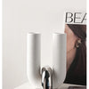 A pair of tall, U-shaped ceramic vessels with metallic accents displayed on a white surface.