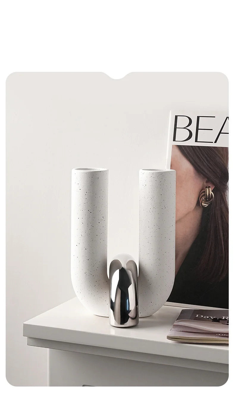 A pair of tall, U-shaped ceramic vessels with metallic accents displayed on a white surface.