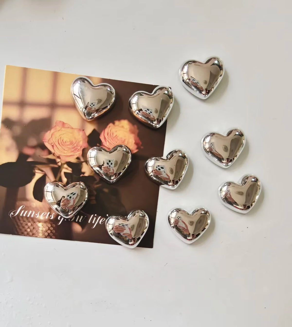 A collection of silver heart-shaped fridge magnets scattered on a white surface.