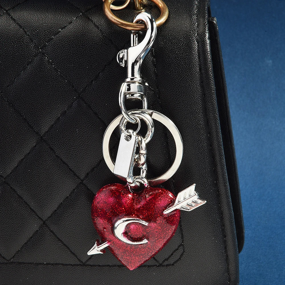 Colgante y dije en forma de corazón plateado, sujeto a un bolso de cuero negro acolchado.