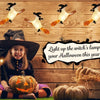 A young girl in a witch costume sits in front of a wooden background decorated with floating LED candles and pumpkins for Hal