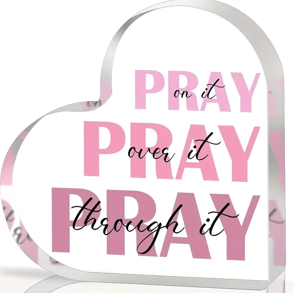 A heart-shaped acrylic sign with pink text that reads Pray on it Pray over it Pray through it