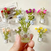 A hand holds several glass jars filled with colorful dried flowers used as decoration.