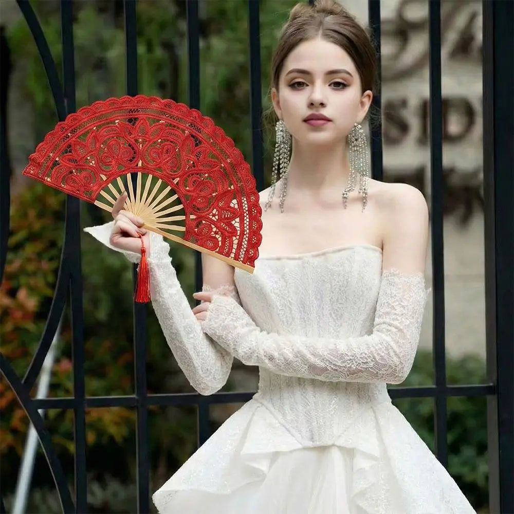 A woman models a vintage red lace hand fan with a tassel pendant and a white dress.