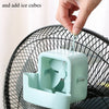 A hand is hanging an ice cube into the housing of a portable ice-cooling floor fan.
