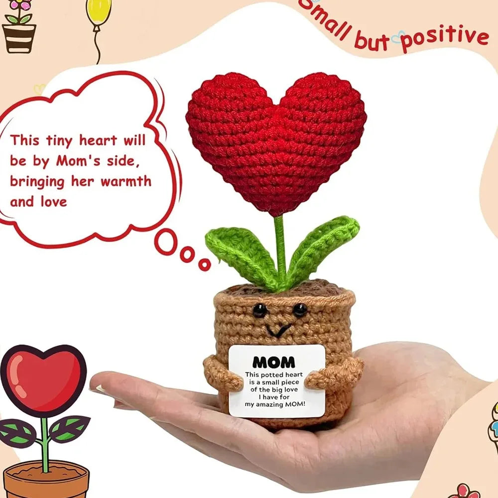 A handcrafted crochet heart plant with a small wooden pot and a note, held in a person's hand.
