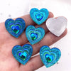 A hand holds a set of twelve heart-shaped blue iridescent peacock resin rhinestone flatbacks.