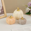 Three ceramic pumpkins in cream and beige tones with gold accents displayed on a white surface.