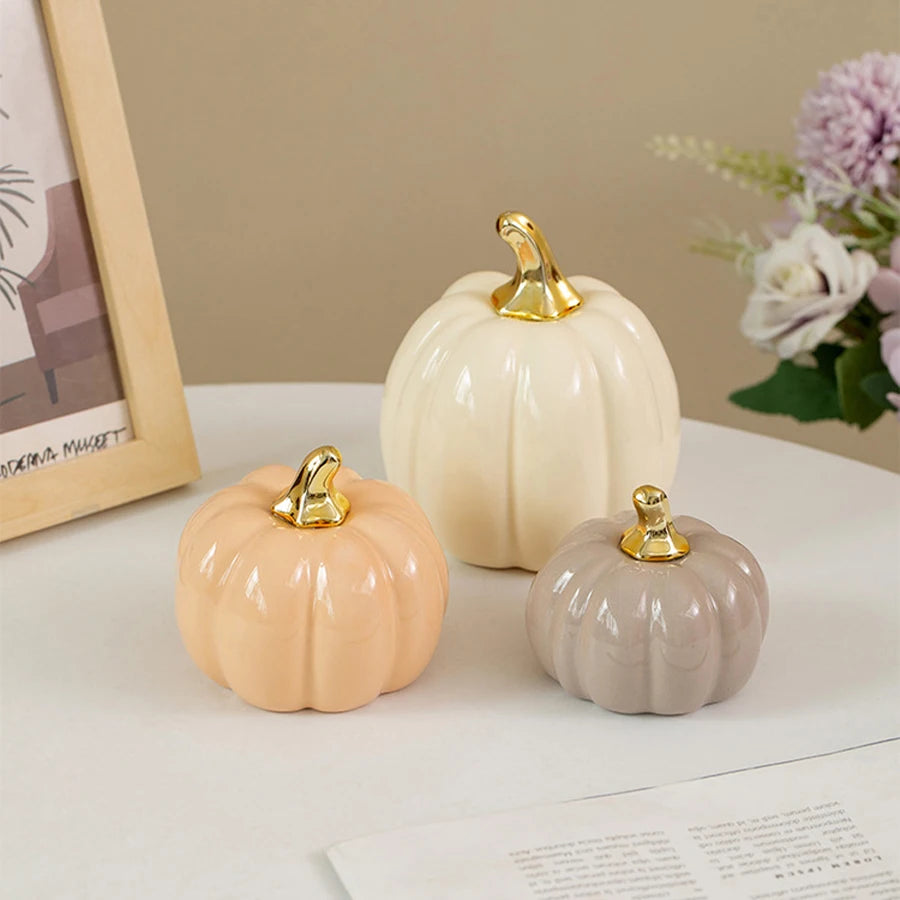 Three ceramic pumpkins in cream and beige tones with gold accents displayed on a white surface.