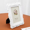 A white ornate frame with a distressed edge holds a pale pink rose floral design on a light background.