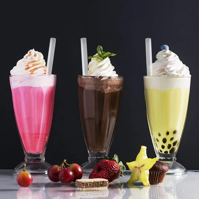 Three glasses of colorful iced drinks topped with whipped cream and garnishes on a reflective surface.