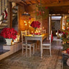 A rustic interior features a wooden dining table set for holiday decor with a bouquet of red poinsettias.