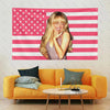 A woman with blonde hair is pictured against an American flag tapestry featuring red and white stripes and stars, displayed i