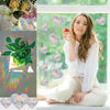 A young woman sits by a window with colorful heart-shaped stickers and green plants visible in the background.