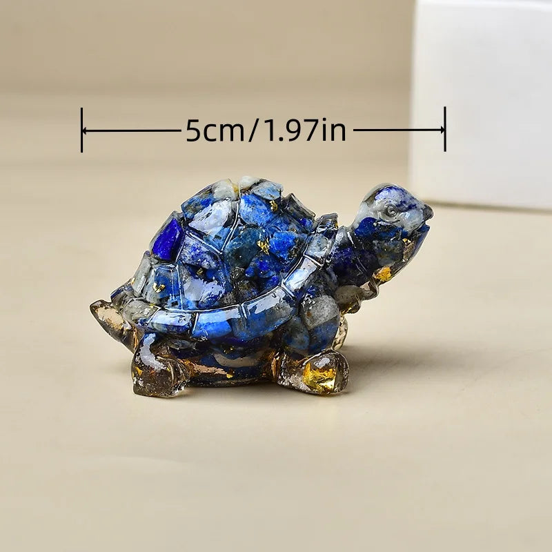 Kleine Kristall-Schildkrötenfigur mit blauen und goldenen Akzenten, vor neutralem Hintergrund.