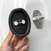 A hand holds a black silicone door lock protector with a silver mounting plate and latch.