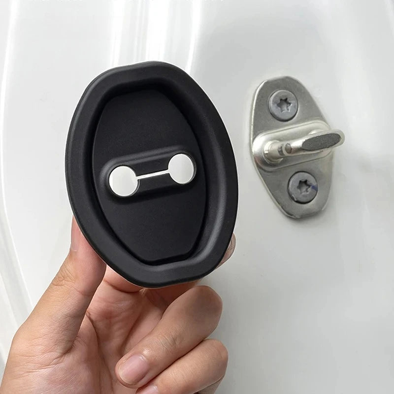 A hand holds a black silicone door lock protector with a silver mounting plate and latch.