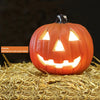 Linterna de calabaza de cerámica naranja con cara sonriente, colocada sobre paja.
