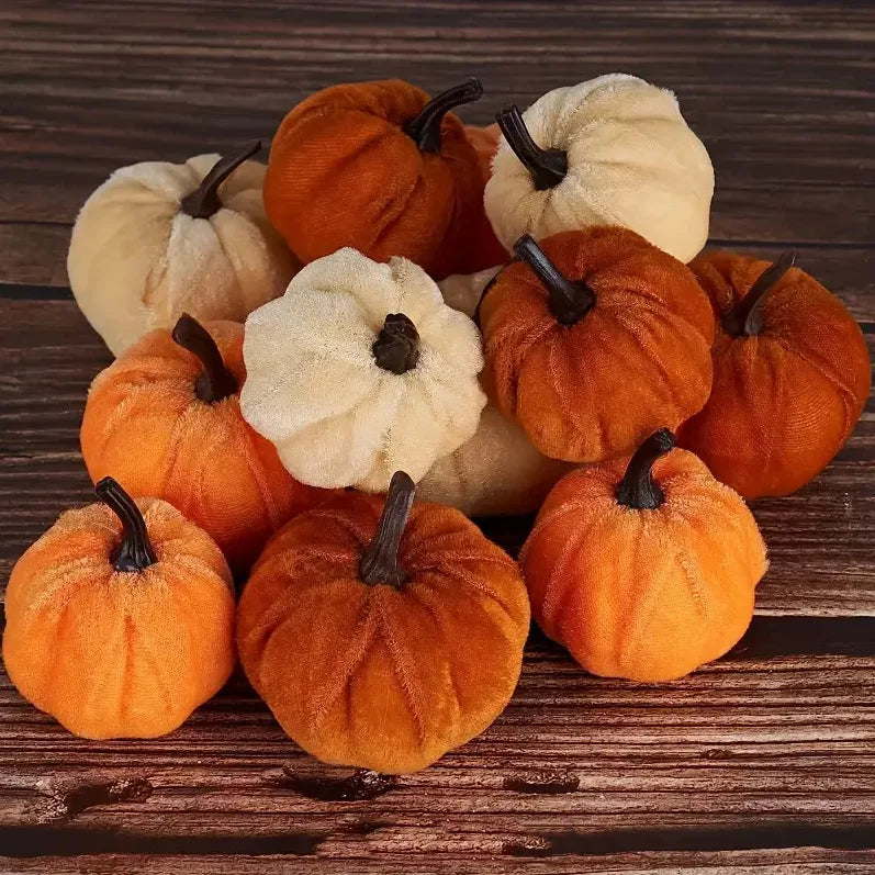 A set of ten velvet pumpkin decorations in shades of orange and cream arranged on a dark wooden surface.