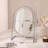 A silver-framed oval vanity mirror with a rotating stand is displayed on a white surface.