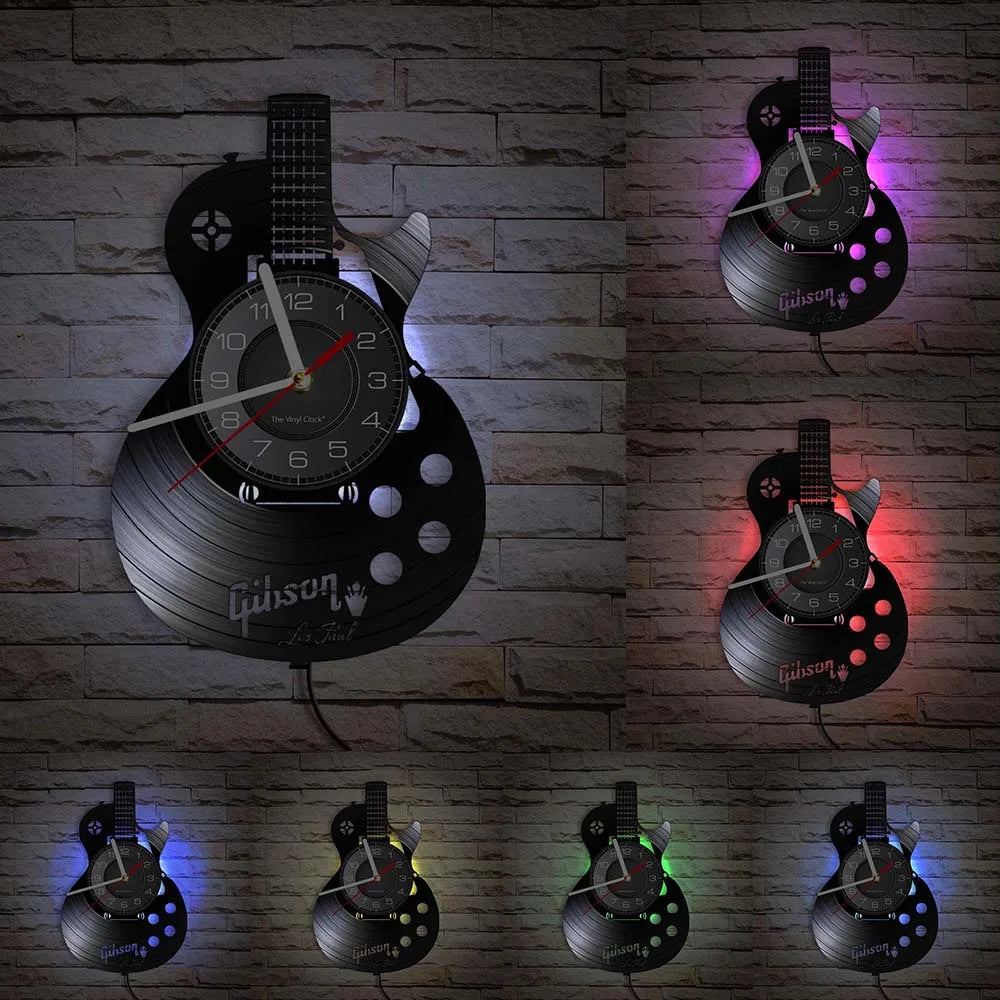 A vintage vinyl record guitar wall clock with a black face and silver disc, displayed against a brick background.