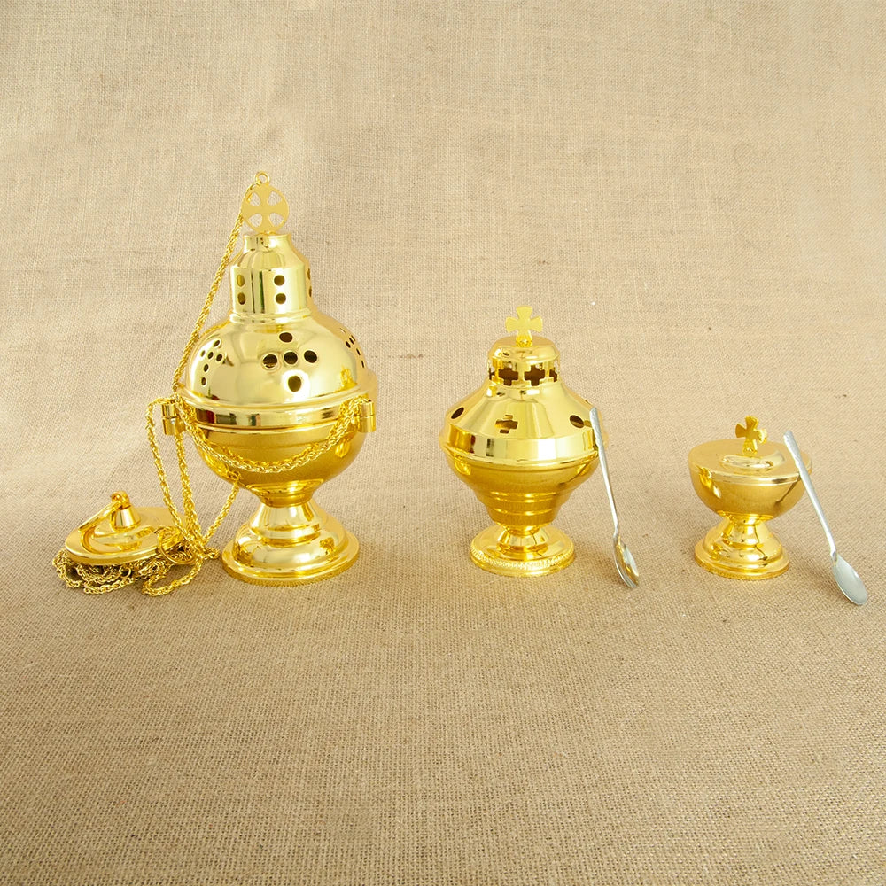 A set of gold-plated Orthodox censers with bells and spoons displayed on a beige fabric background.