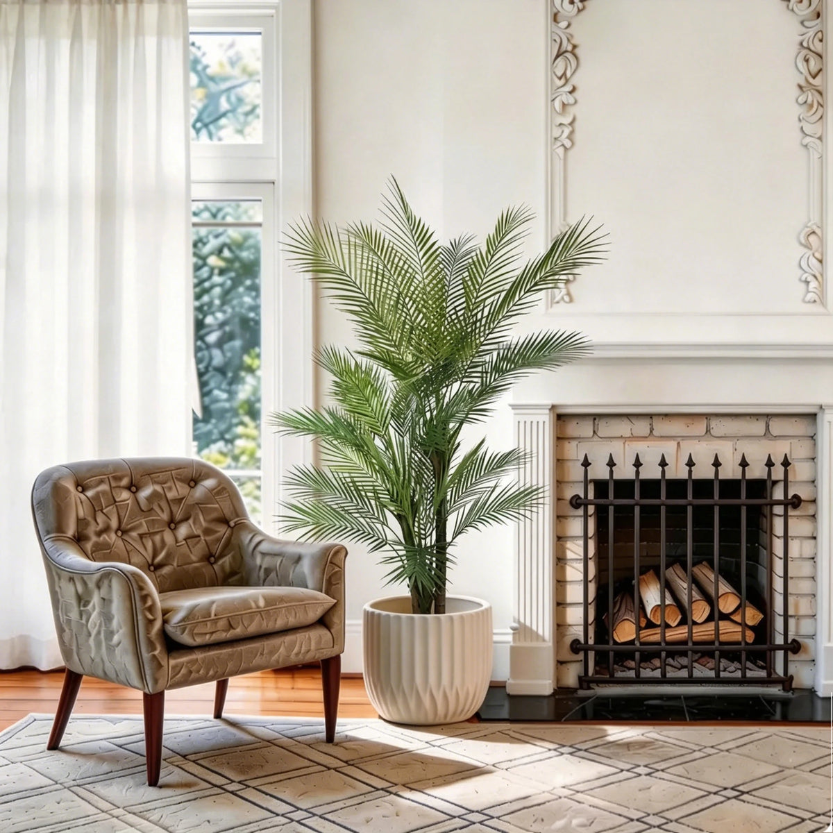 An artificial triple trunk palm tree in a beige pot stands in a bright living room next to a fireplace.