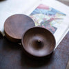 A dark brown solid wood incense stick burner with a round lid resting on a book.