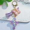 A gold-toned keychain featuring a purple tassel and a pink glitter butterfly charm with a purple resin cross.