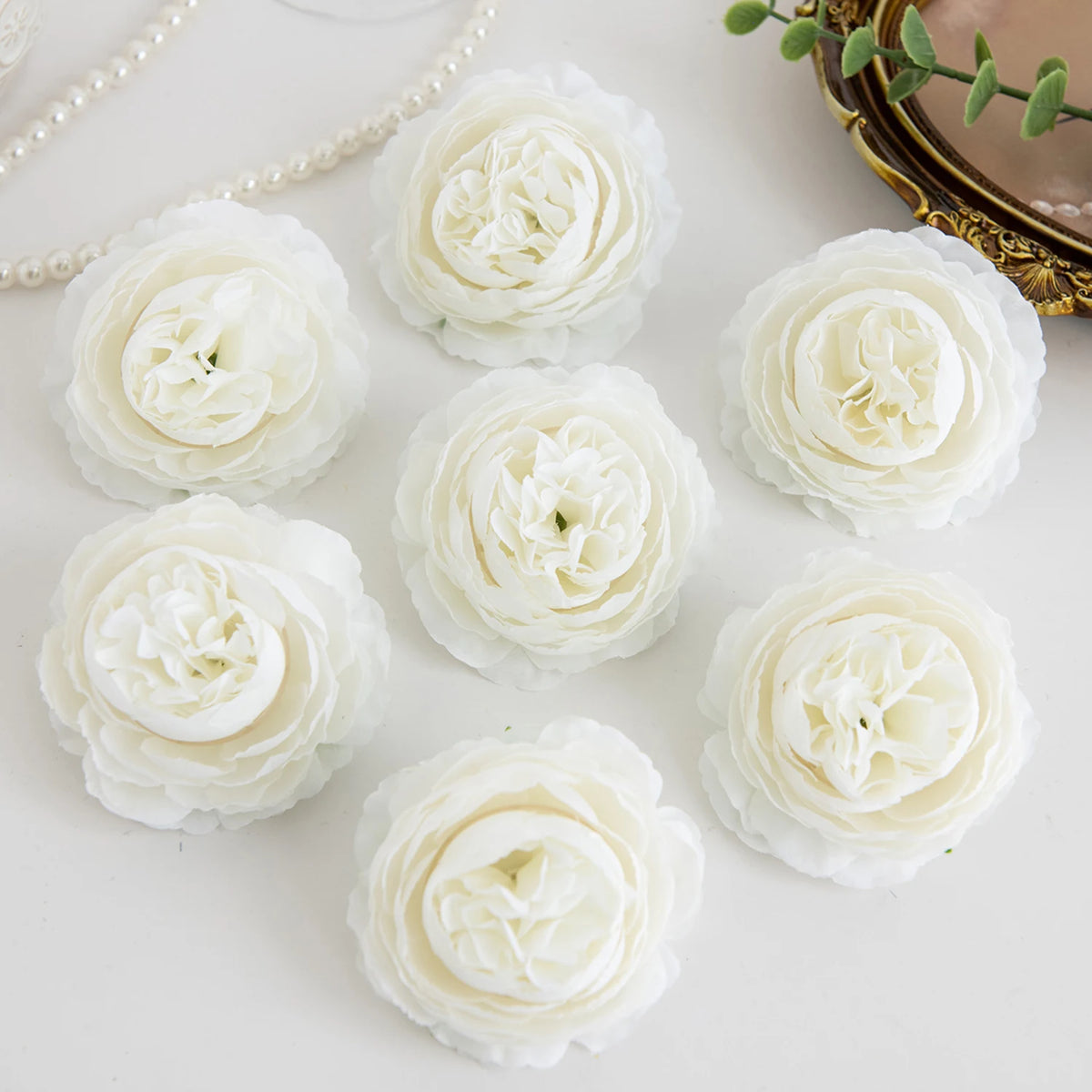 A collection of white silk peony artificial flowers arranged on a white surface.