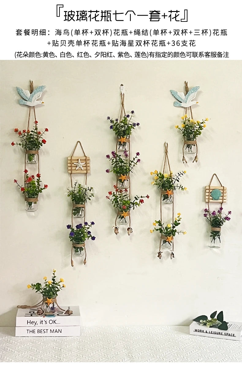 A display of various potted flowers and greenery arranged in hanging glass terrariums on a white wall.