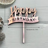 A pink acrylic birthday cake topper featuring the words Happy Birthday on a banner shape.