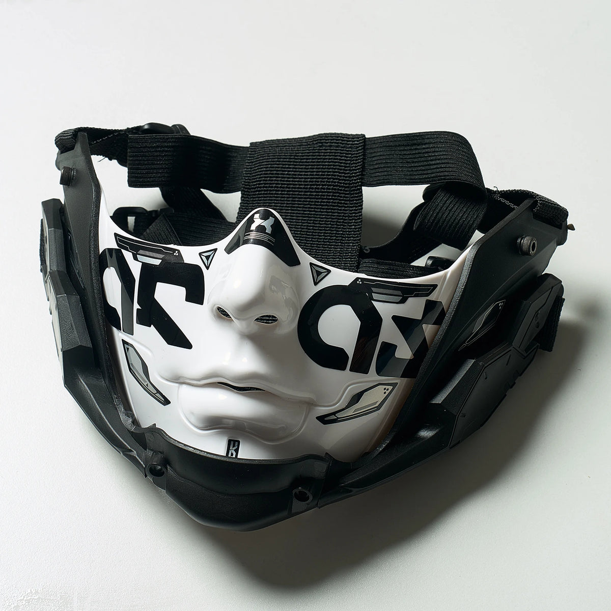 A black half face mask with a white stylized face design and black straps.