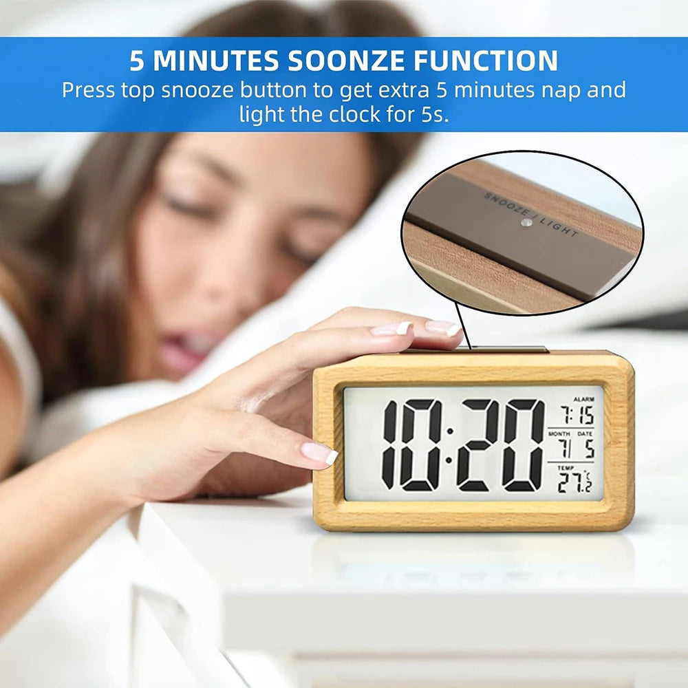A hand presses a snooze button on a wooden digital alarm clock displaying 10:20, with a woman sleeping in the background.