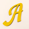 A gold 3D acrylic letter wall sticker in a cursive style.