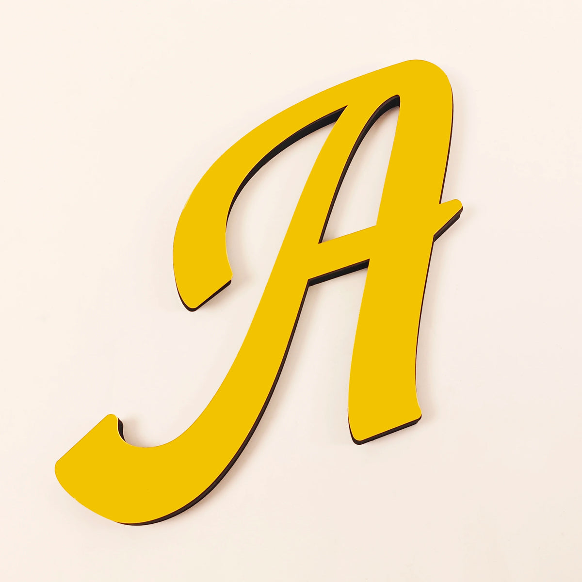 A gold 3D acrylic letter wall sticker in a cursive style.