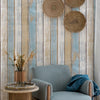 A vintage blue and white plank wallpaper features rustic wood textures and woven natural fiber wall hangings above a gray arm