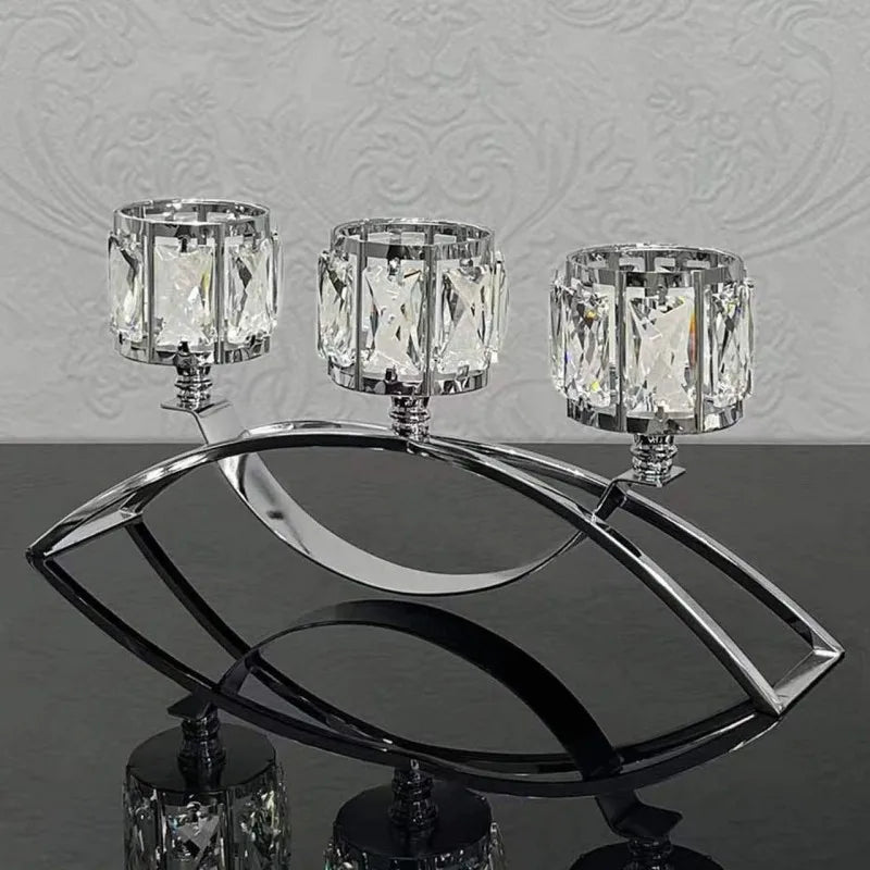 Three-arm gold crystal candelabra with three glass candle holders displayed on a reflective surface.