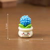 A small white ceramic pot with a bright blue, textured flower on top, used as a craft or dollhouse decoration.