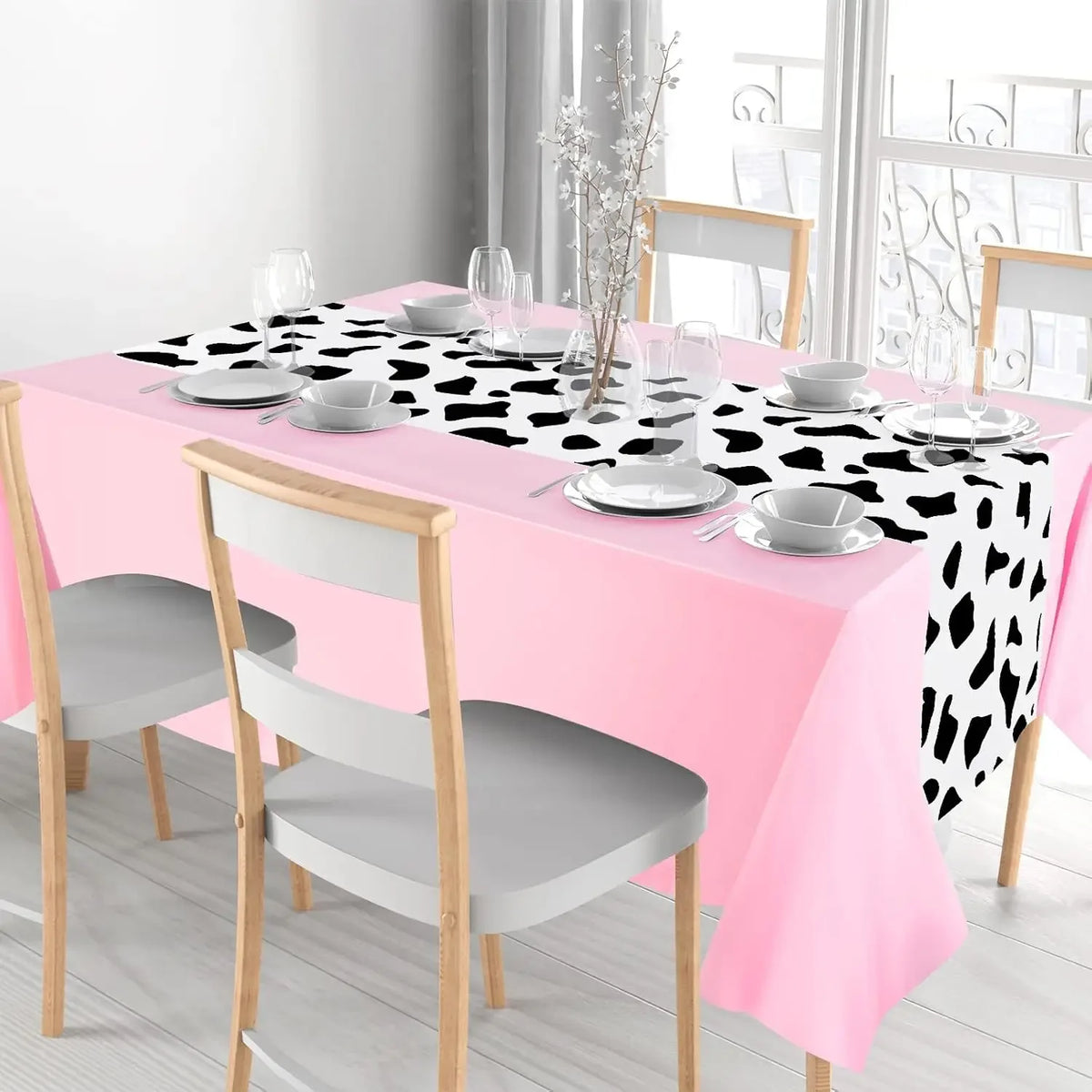 A pink cow print western tablecloth set for parties featuring a table, plates, and silverware.