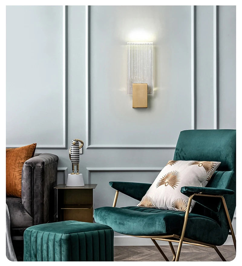 Modern bubble crystal LED wall sconces mounted on a light gray wall above a dark green velvet chair.