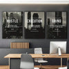 A set of three framed wall art prints featuring motivational text Hustle Execution and Grind displayed above a wooden desk.