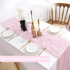 Pink cheesecloth table runner with white plates and silverware on a white table.