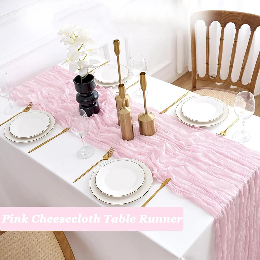 Pink cheesecloth table runner with white plates and silverware on a white table.